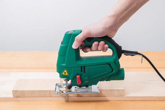 Un hombre trabaja con una sierra de calar eléctrica para madera sobre una mesa de madera con y sin guantes y mide con una cinta métrica