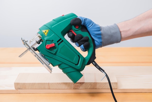 Un hombre trabaja con una sierra de calar eléctrica para madera sobre una mesa de madera con y sin guantes y mide con una cinta métrica