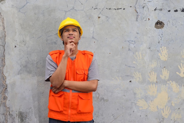 Hombre trabajador de la construcción toca el mentón mirando hacia arriba piensa en una nueva idea para la construcción de obras como reparación