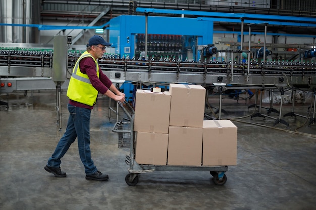 Hombre trabajador de fábrica tirando carro de cajas de cartón