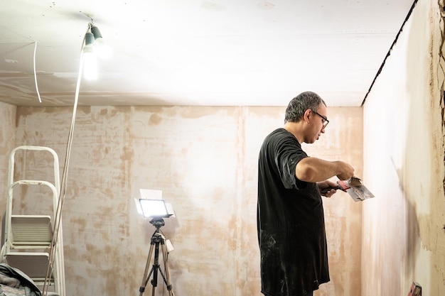 Hombre trabajador feliz haciendo pared en la habitación a mano reparación de espátula