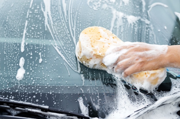 Hombre trabajador de la gente sosteniendo la ventana limpiadora de espuma de burbuja y esponja amarilla de mano para lavar el coche. Concepto de lavado de coches limpio. Deje espacio para escribir mensajes.