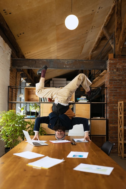 Hombre trabajador de oficina de pie sobre la cabeza en la mesa de trabajo haciendo estiramientos descansando del trabajo