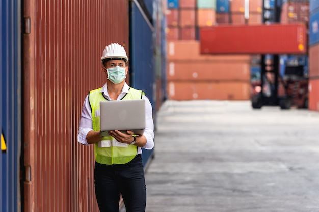 Hombre trabajador Portrit usando una computadora portátil waring mascarilla quirúrgica y cabeza blanca de seguridad para proteger contra la contaminación y los virus en el lugar de trabajo durante la preocupación por la pandemia de covid