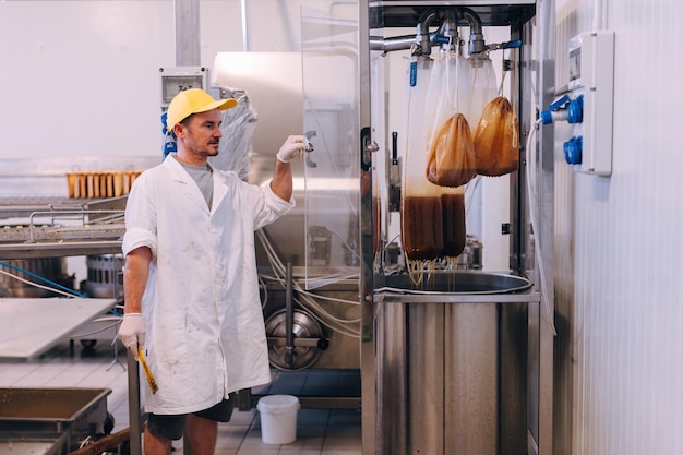 Foto hombre trabajador revisando la máquina de procesamiento de miel en la fábrica de la industria apícola de la casa de la miel