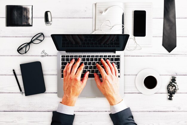 Hombre trabajador con taza de café para computadora portátil y otros accesorios en maqueta de mesa de madera blanca