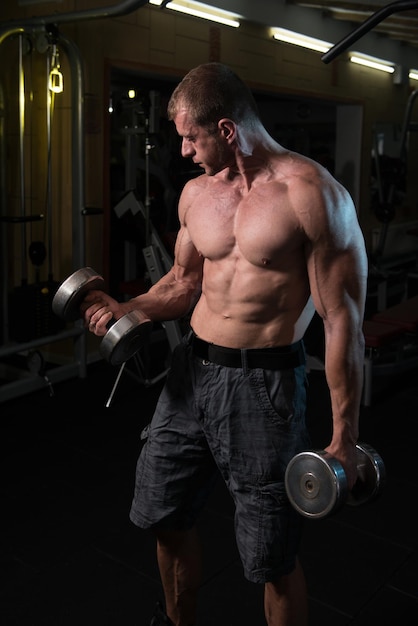 Hombre trabajando bíceps en el gimnasio Curls de concentración con mancuernas