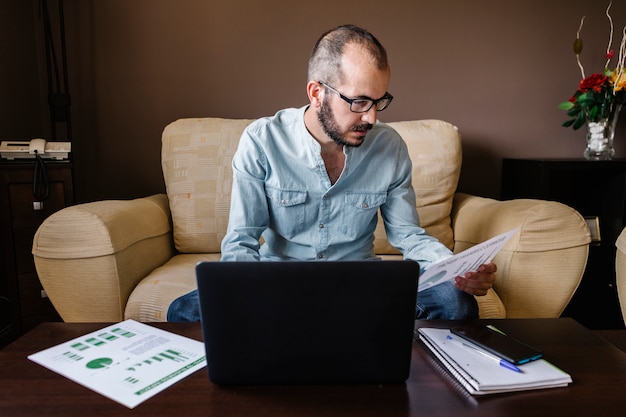 Hombre trabajando en la computadora portátil desde casa y analizando datos financieros con gráficos y tablas