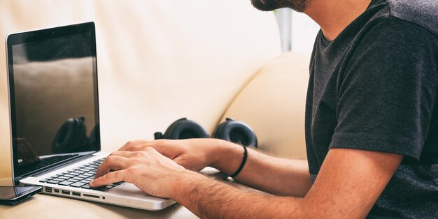 Hombre trabajando con una laptop sentada en un sofá en casa