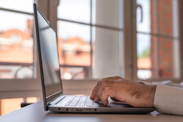 Hombre trabajando en una laptop en su casa con grandes ventanales de luz