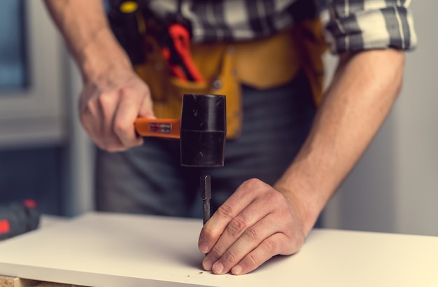 Hombre trabajando con martillo y broca para agujero durante el proceso de fabricación de muebles de madera