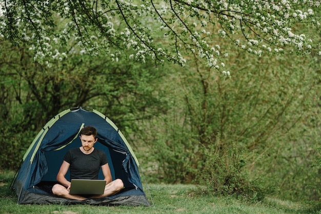 Hombre trabajando con un portátil en la carpa en la naturaleza