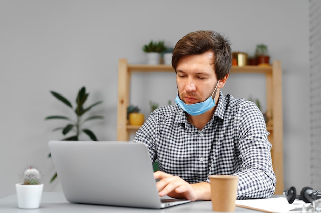 Hombre trabajando en un portátil en casa y con máscara médica