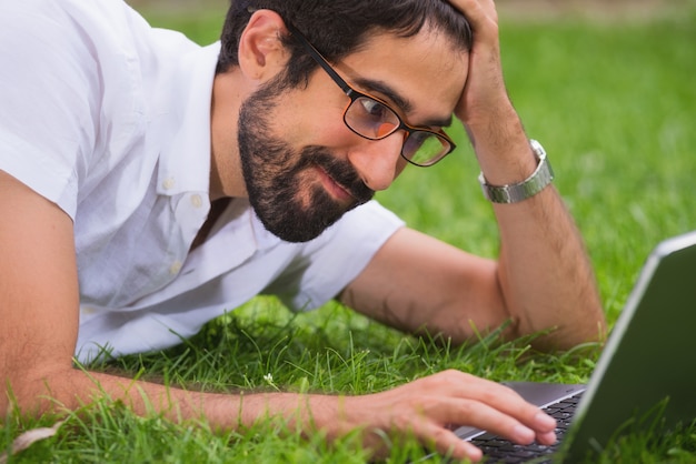 hombre trabajando en su computadora portátil tirado en el césped del parque expresión feliz