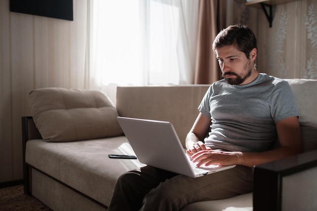 Hombre de trabajo remoto trabajando en una computadora portátil sentado en un sofá en casa