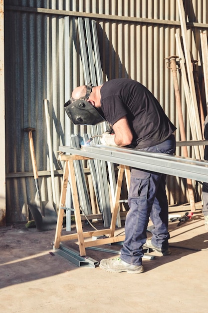 Hombre en el trabajo soldando una barra de hierro con protección facial