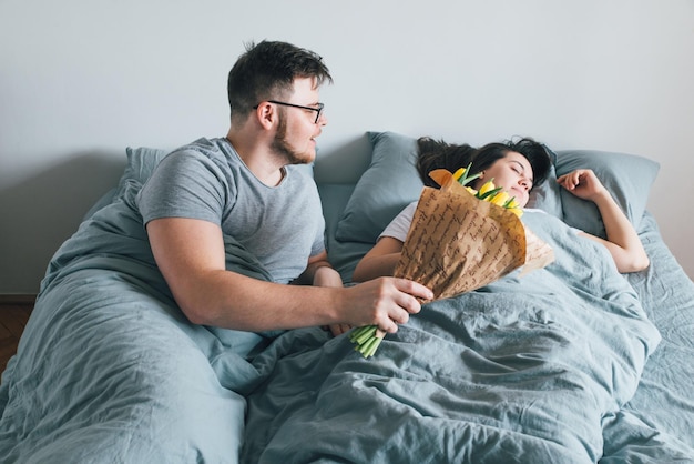 El hombre trae flores en la cama sorpresa para la novia en el concepto romántico de la mañana