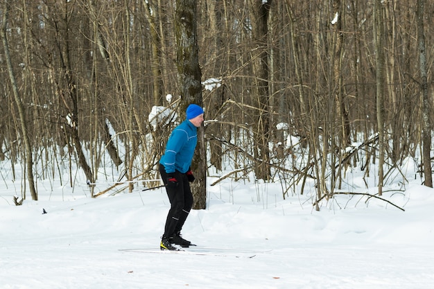 Hombre en un traje azul se ejecuta en esquís en el bosque de invierno.