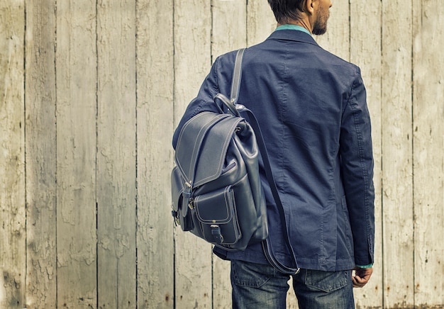 Foto hombre en traje azul y jeans con mochila de cuero.