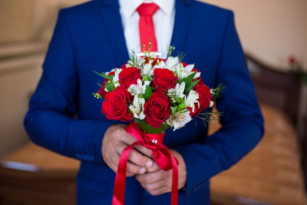 Un hombre con un traje azul con un ramo de rosas rojas