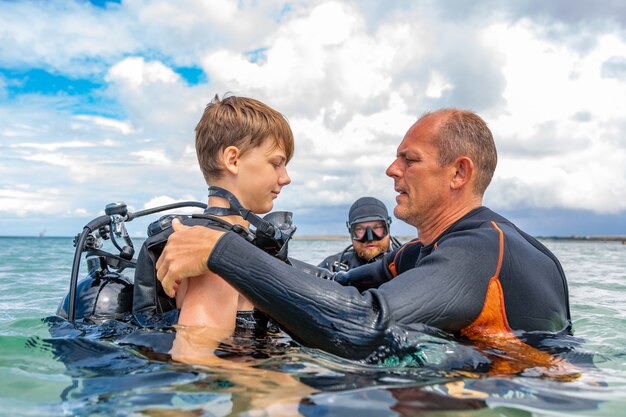 Un hombre en traje de buceo prepara a un niño para bucear