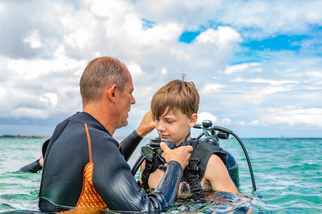 Un hombre en traje de buceo prepara a un niño para bucear