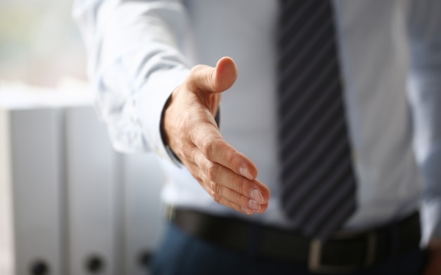 Hombre en traje y corbata dan la mano como hola en primer plano de la oficina