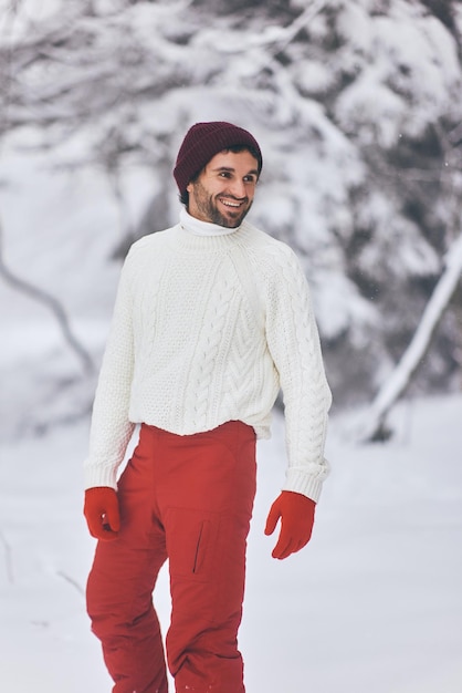 Hombre en traje de esquí y suéter en el bosque nevado durante las vacaciones de invierno al aire libre