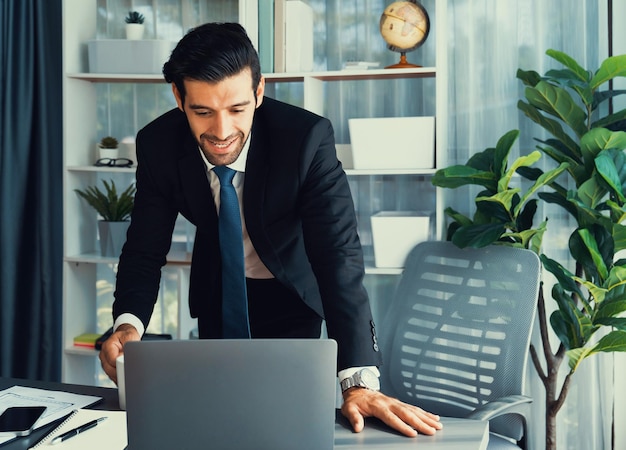 Un hombre con traje está mirando una computadora portátil en una oficina.