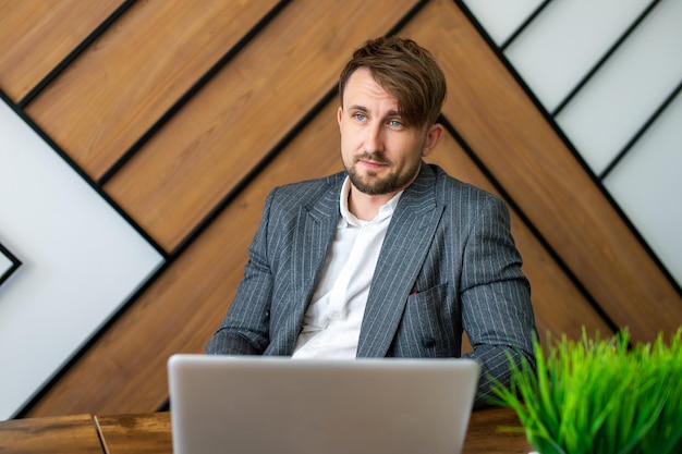 Un hombre con traje está sentado en su lugar de trabajo mirando una computadora portátil y riendo