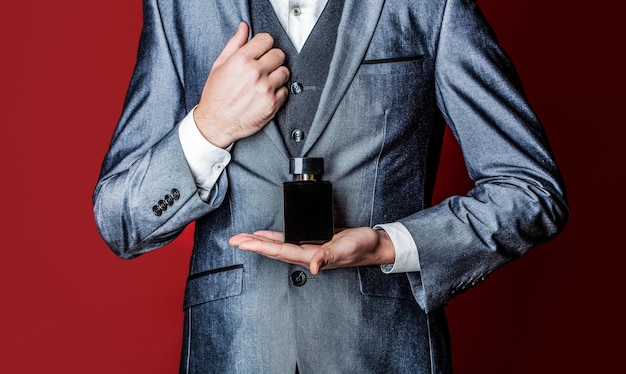 Hombre en traje formal botella de perfume primer plano Hombre sosteniendo una botella de perfume Hombres perfume en la mano sobre fondo de traje Olor a fragancia