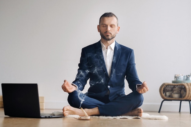 Foto un hombre con traje formal medita mientras está sentado en un gimnasio con una computadora portátil