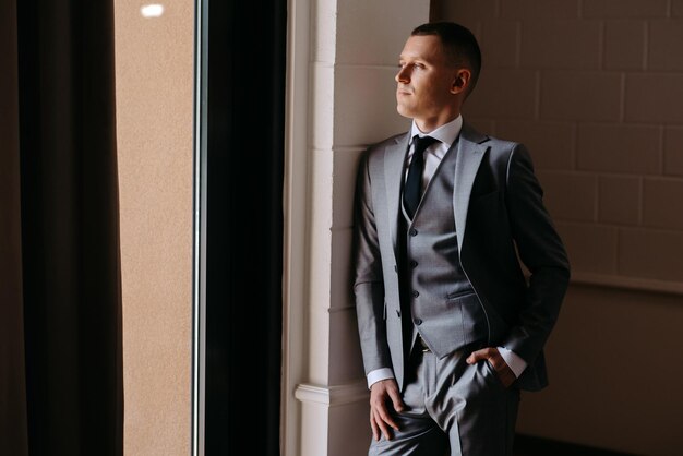 Foto un hombre con un traje gris de pie frente a una ventana