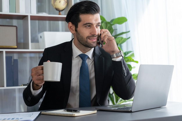 Un hombre con traje hablando por teléfono mientras usa una computadora portátil.