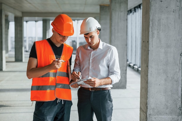 El hombre de traje y manitas con ropa protectora naranja está trabajando en la construcción