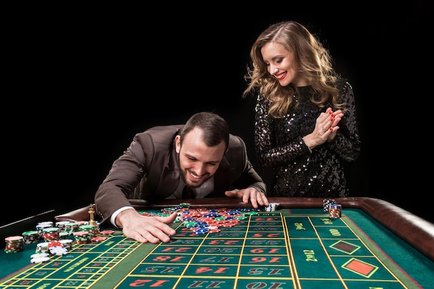 Un hombre con un traje marrón con una mujer hermosa con un vestido negro está jugando en una mesa de ruleta en un casino. Emoción de los jugadores de juego