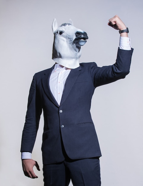 Un hombre con un traje y una máscara de caballo sobre un fondo claro. Fondo conceptual de negocios
