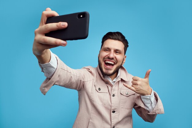 Hombre en traje de moda sonriendo y mostrando el pulgar hacia arriba signo mientras toma selfie