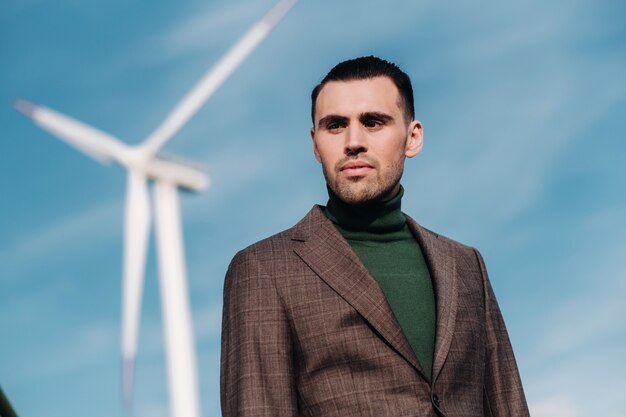 Un hombre en un traje de negocios con una camisa de golf verde se encuentra junto a un molino de viento contra el fondo