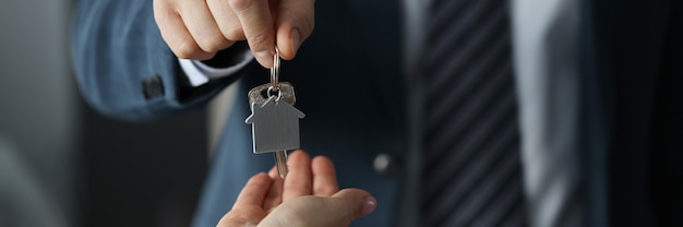 Hombre en traje de negocios entrega las llaves de la casa al primer plano de la mujer. Asistencia social en concepto de construcción