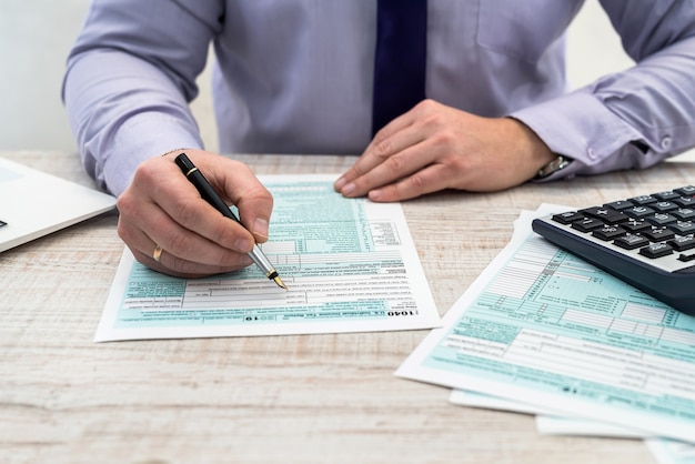 Un hombre en traje de negocios escribe un formulario de impuestos 1040 en la oficina. Las manos masculinas se llenan de papel con la calculadora en el lugar de trabajo. Concepto de contabilidad