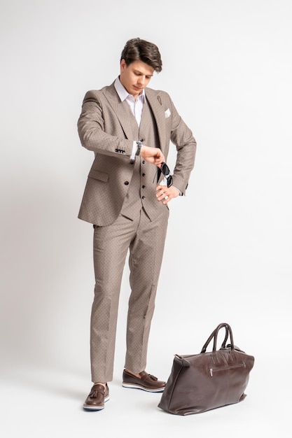 Un hombre con traje de negocios mira su reloj mientras está de pie junto a una gran bolsa de viaje