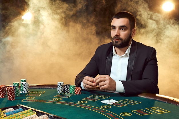 Un hombre en traje de negocios sentado en la mesa de juego. Jugador masculino. Pasión, cartas, fichas, alcohol, dados, juegos de azar, casino: es como entretenimiento masculino.