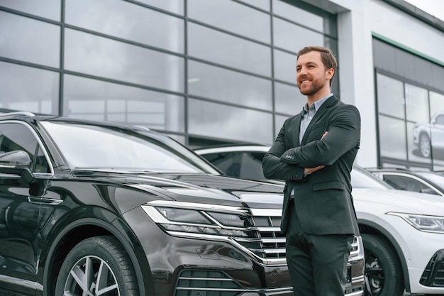 Hombre de traje negro está al aire libre cerca de coches modernos Concepto de venta de negocios