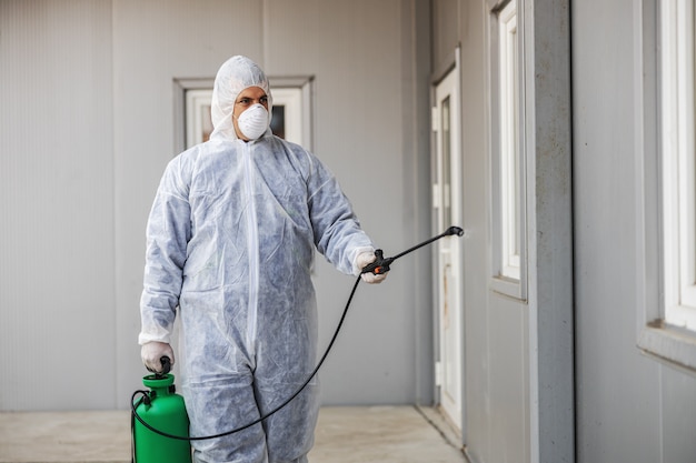 Foto hombre con traje de protección contra virus y máscara desinfectando edificios de coronavirus con el rociador. epidemia.