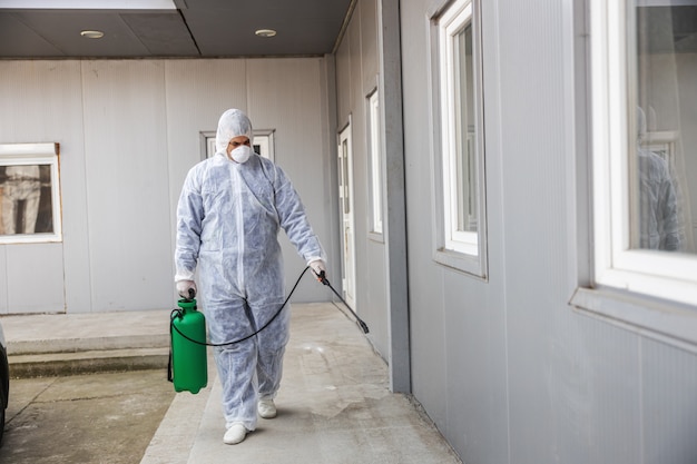 Hombre con traje de protección contra virus y máscara desinfectando edificios de coronavirus con el rociador. epidemia.