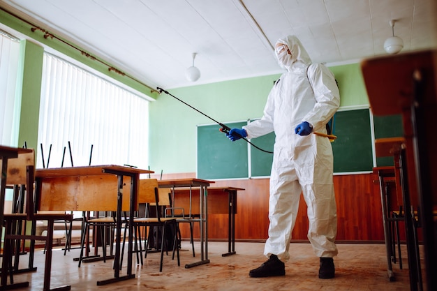 Hombre en un traje de protección desinfectando un aula