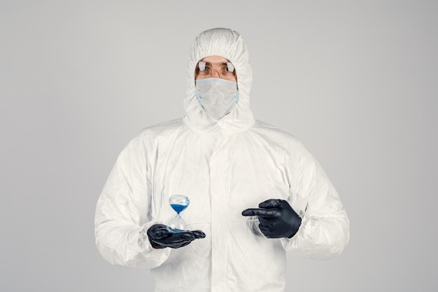 Foto un hombre con un traje protector blanco, una máscara de fondo blanco con un reloj en las manos. una pandemia epidémica es un nuevo virus que se propaga rápidamente, un concepto médico.