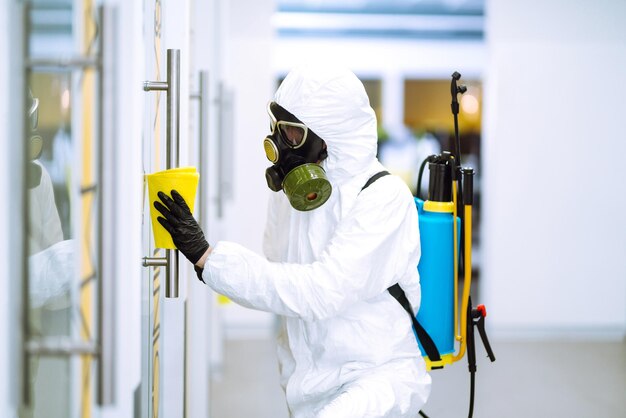 El hombre con traje protector de materiales peligrosos lava los muebles de oficina para prevenir la propagación del coronavirus.