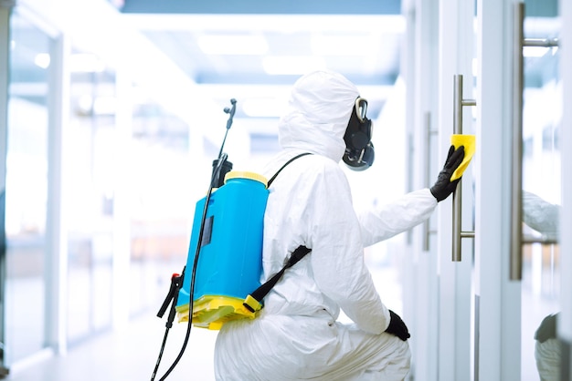 El hombre con traje protector de materiales peligrosos lava los muebles de oficina para prevenir la propagación del coronavirus.